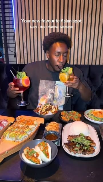 Gast drinkt een mocktail aan een tafel met een sushiboot, bao buns en gerechten
