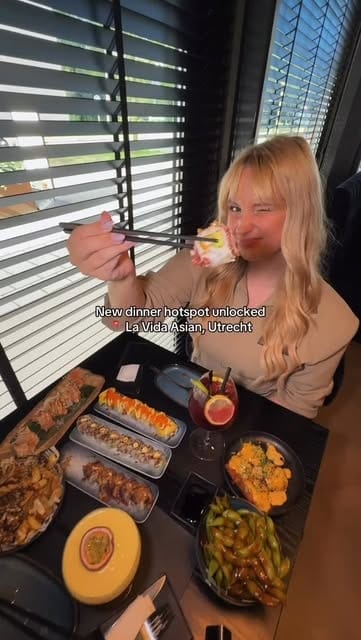Gast met eetstokjes aan een tafel vol sushirolls, edamame en een passievrucht-mocktail