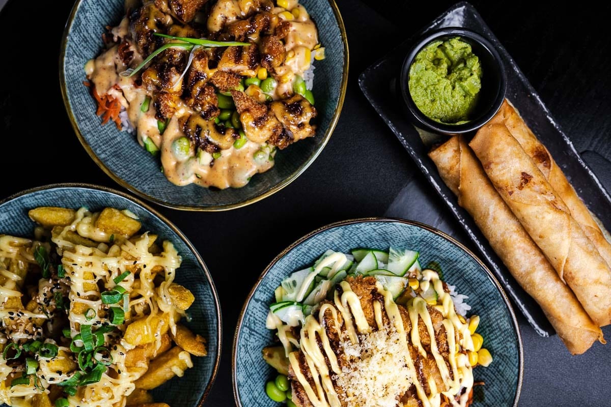 Bovenaanzicht van gevulde bowls en loempia's met groene dipsaus op een donkere tafel